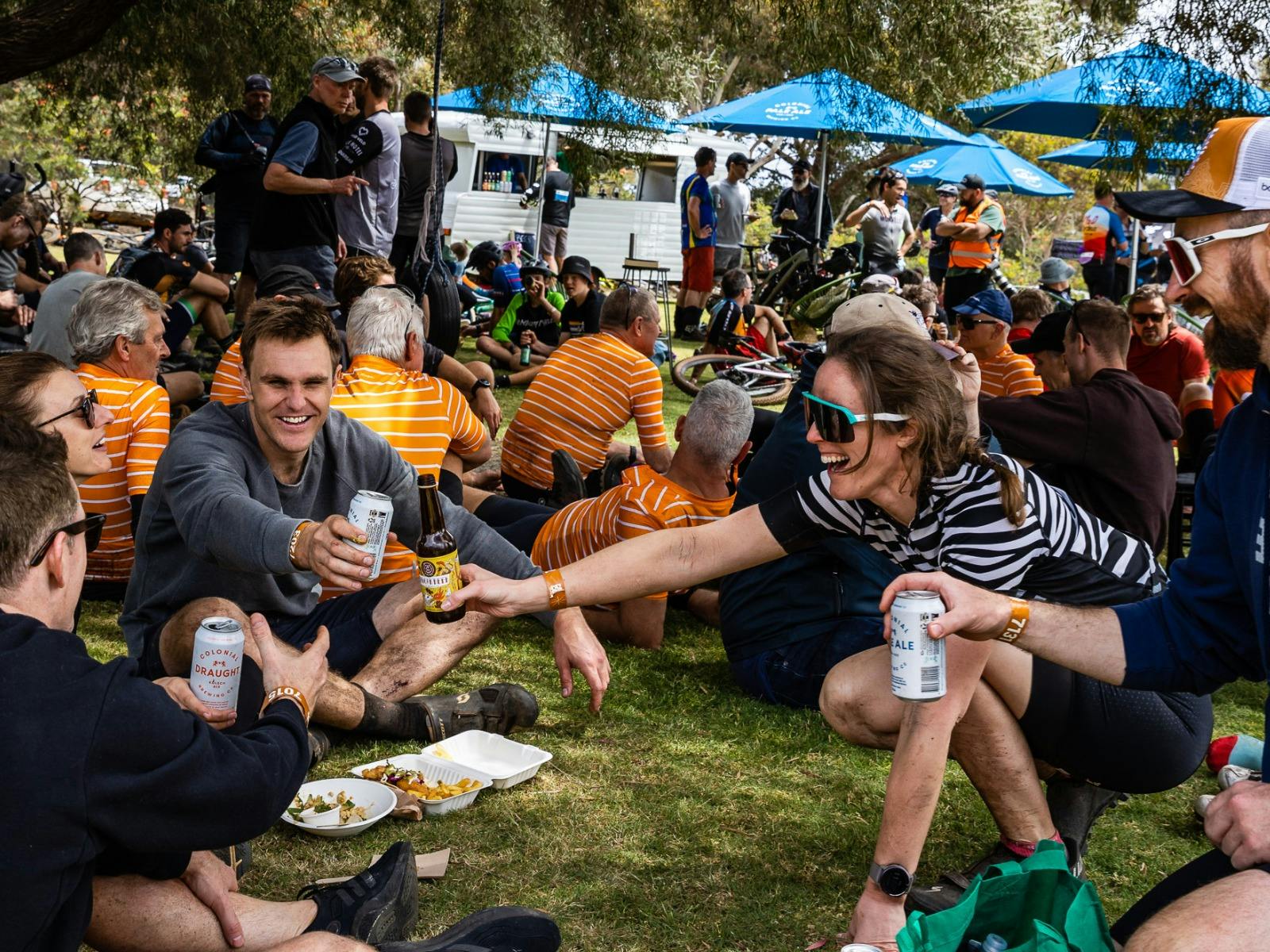 Group of riders sitting in a circle on the ground, celebrating post event with beers and food