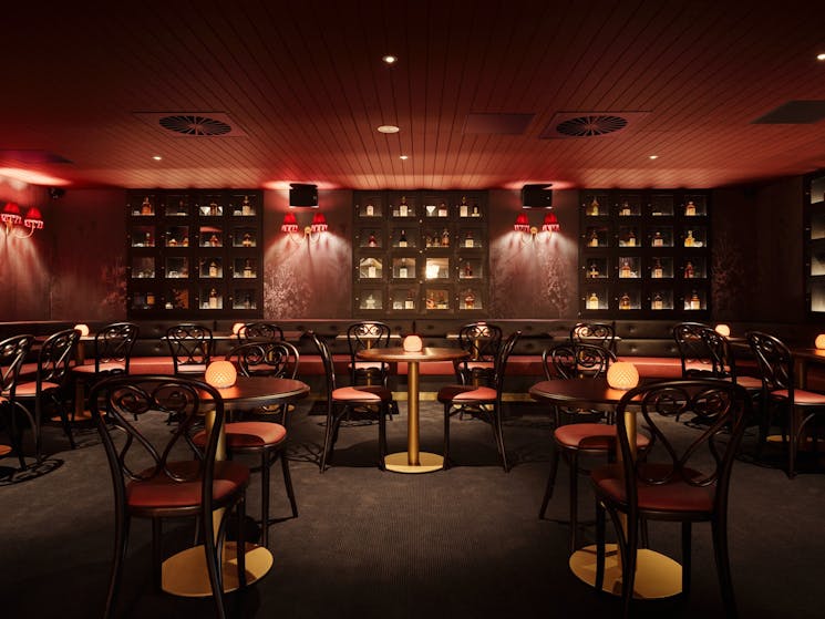 A red room filled with tables, chairs an lamps. The walls are lined with glass boxes with whisky