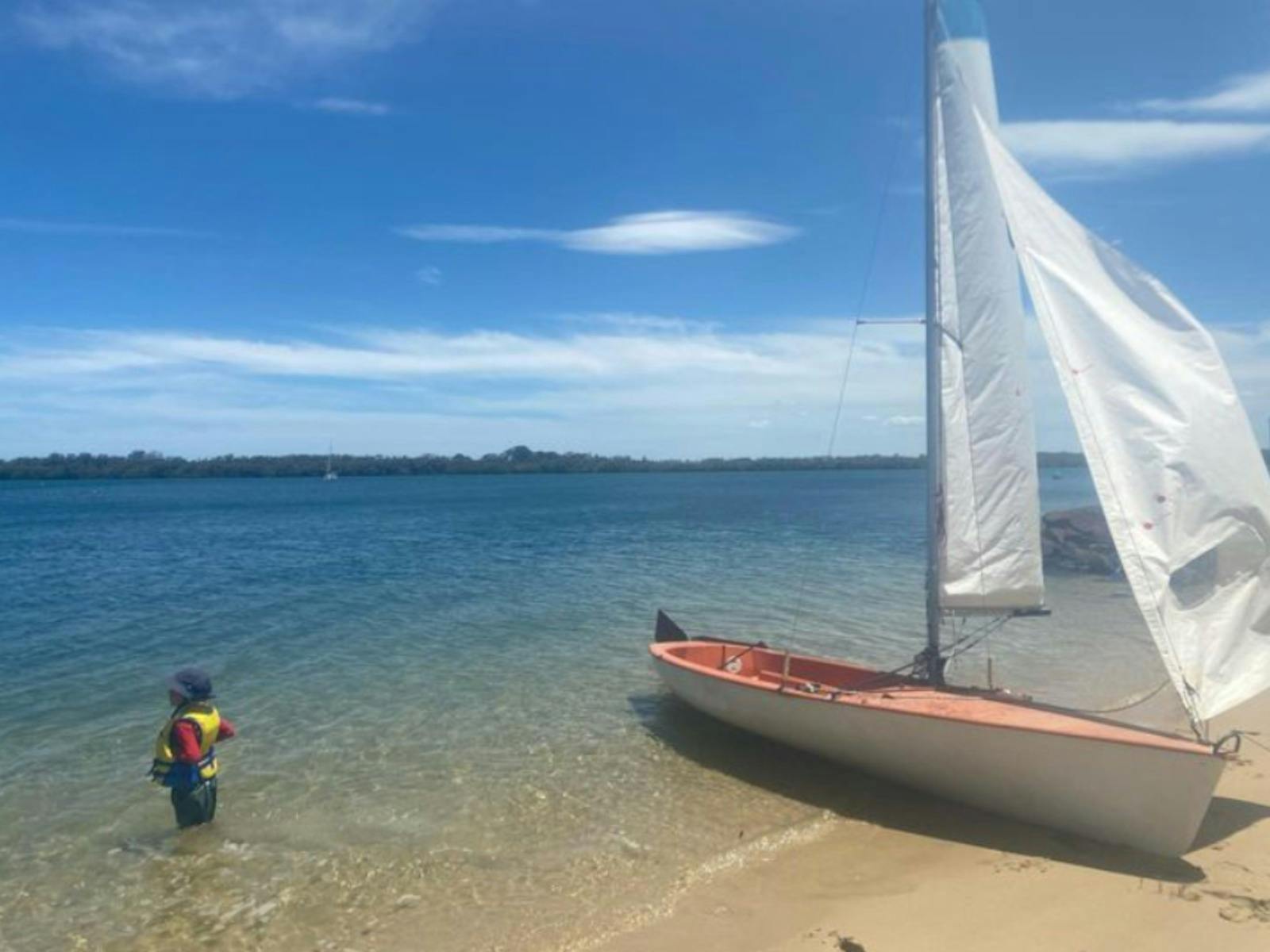 a sailboat on the edge of the Richmond River with a small boy standing close by