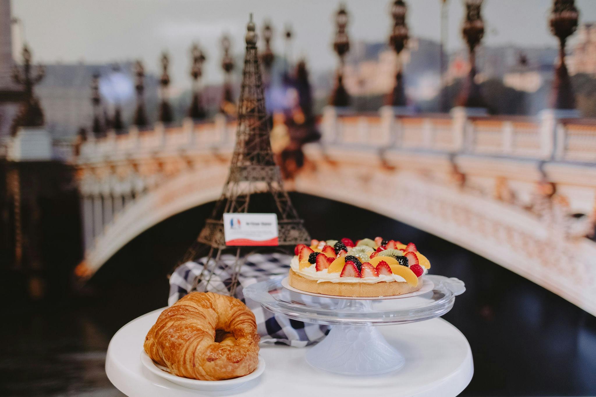 Table setting with a crossaint, a fruit flan and a statue of the Eiffel Tower in the background.
