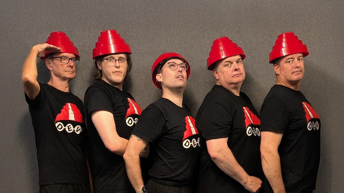 Five caucasian men of varying ages dressed in black t-shirts with red traffic cone style hats