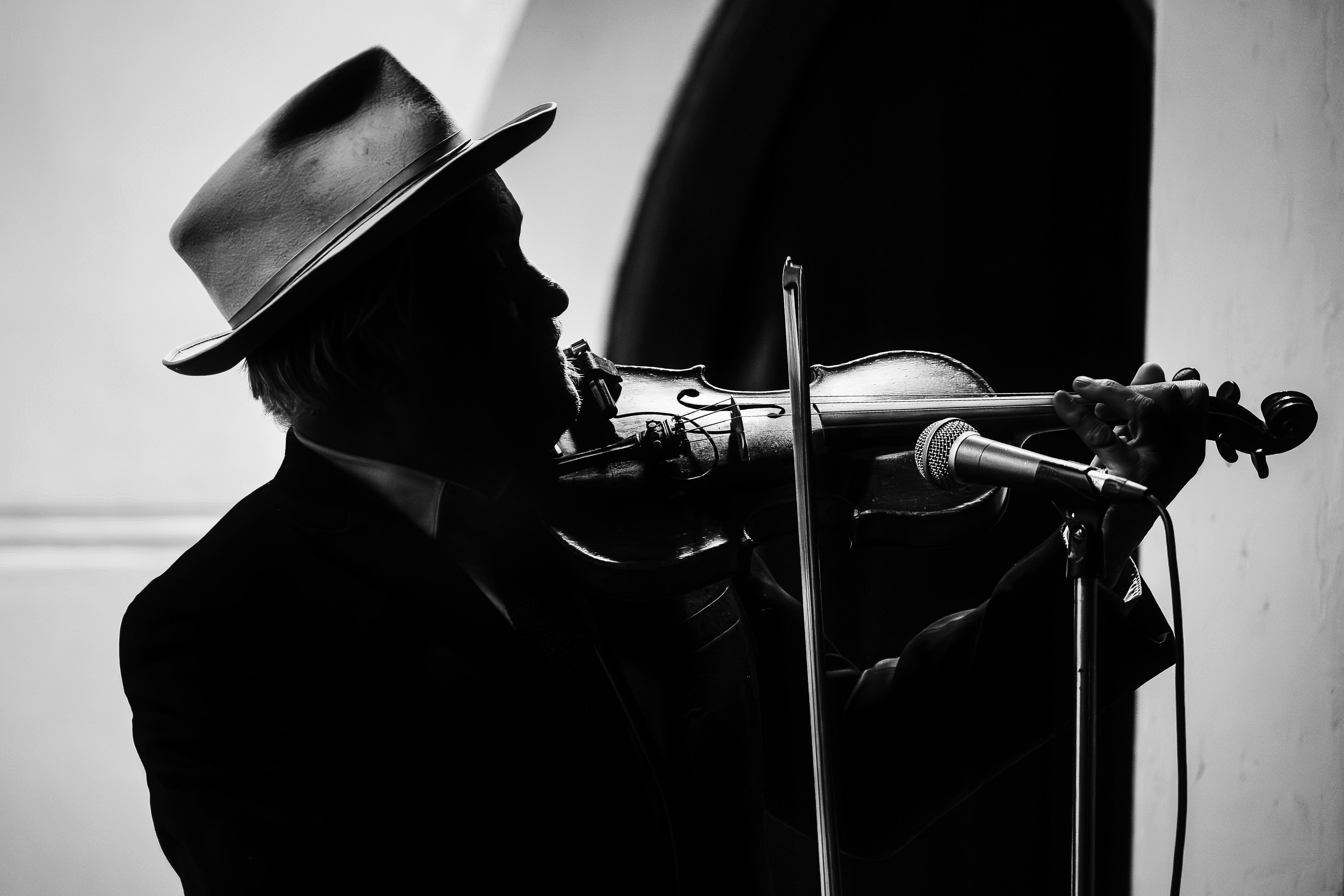 Black and white image of a man wearing a fedora and in silhouette playing a violin