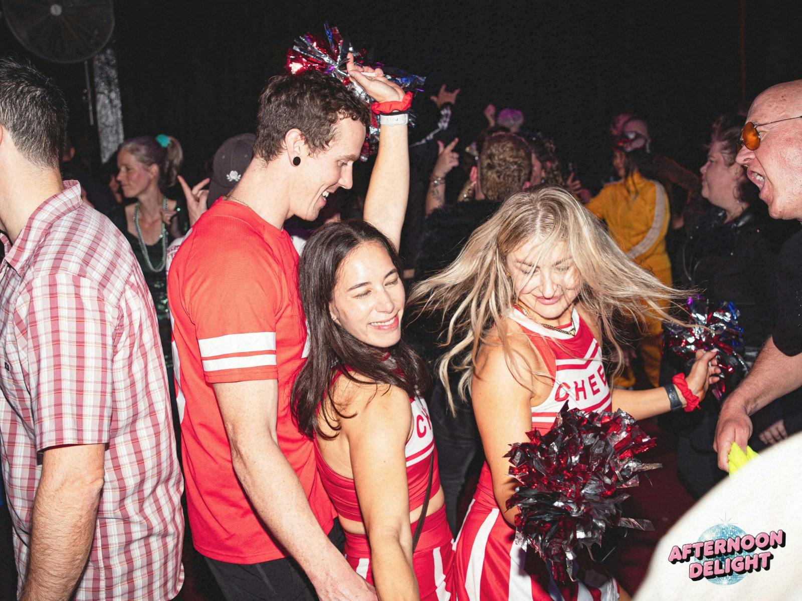 Image shows people dressed in cheerleader outfits dancing in an energetic crowd