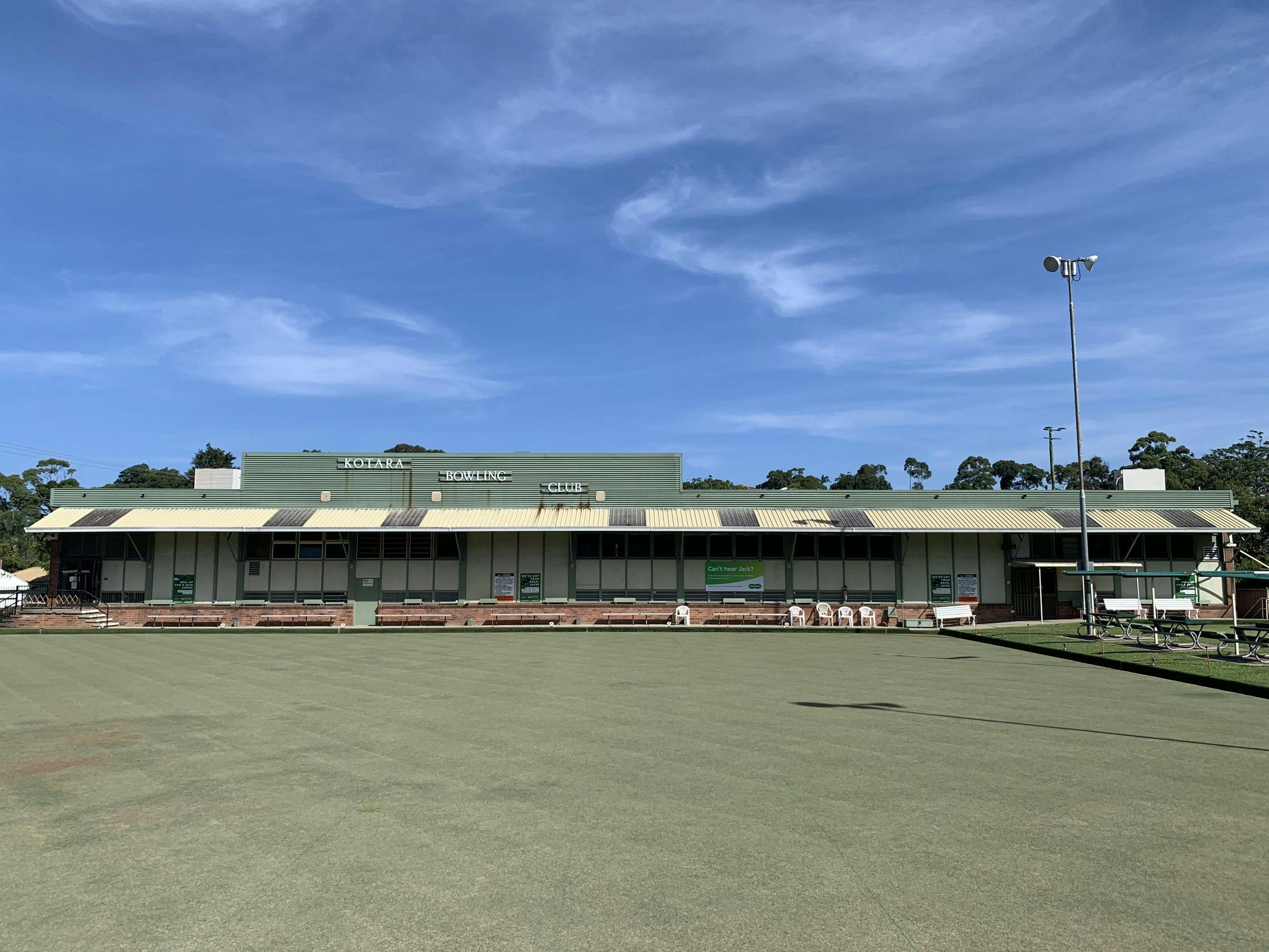 Club Kotara clubhouse viewed across the bowling green under a blue sky.