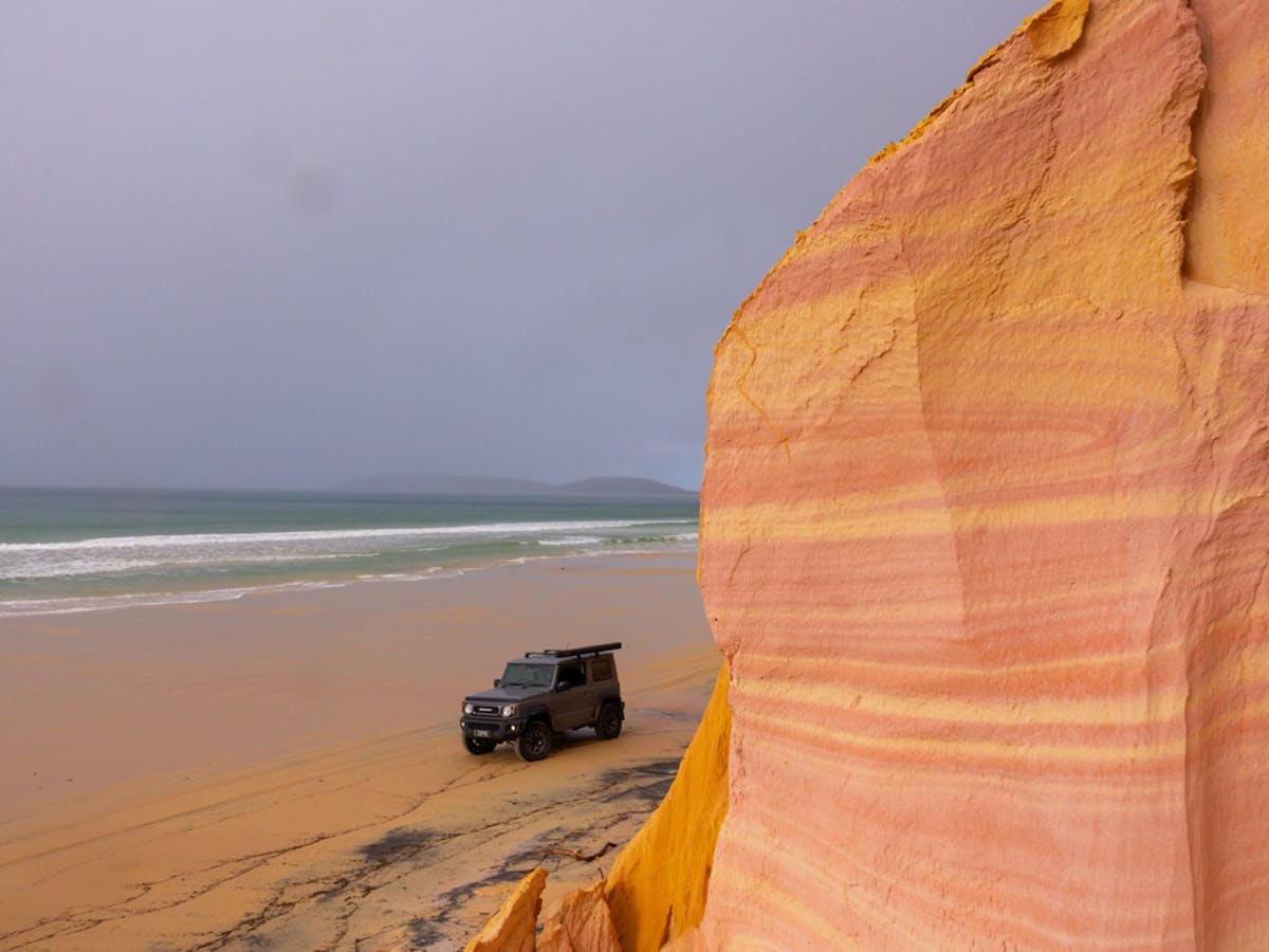 Car on the beach with the red coloured cliffs at Rainbow beach Car on the beach with the red coloured cliffs at Rainbow beach