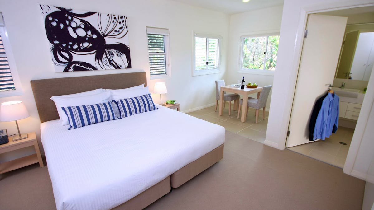 Studio apartment with king bed, blue striped cushions, dining table, ensuite bathroom and kitchenett