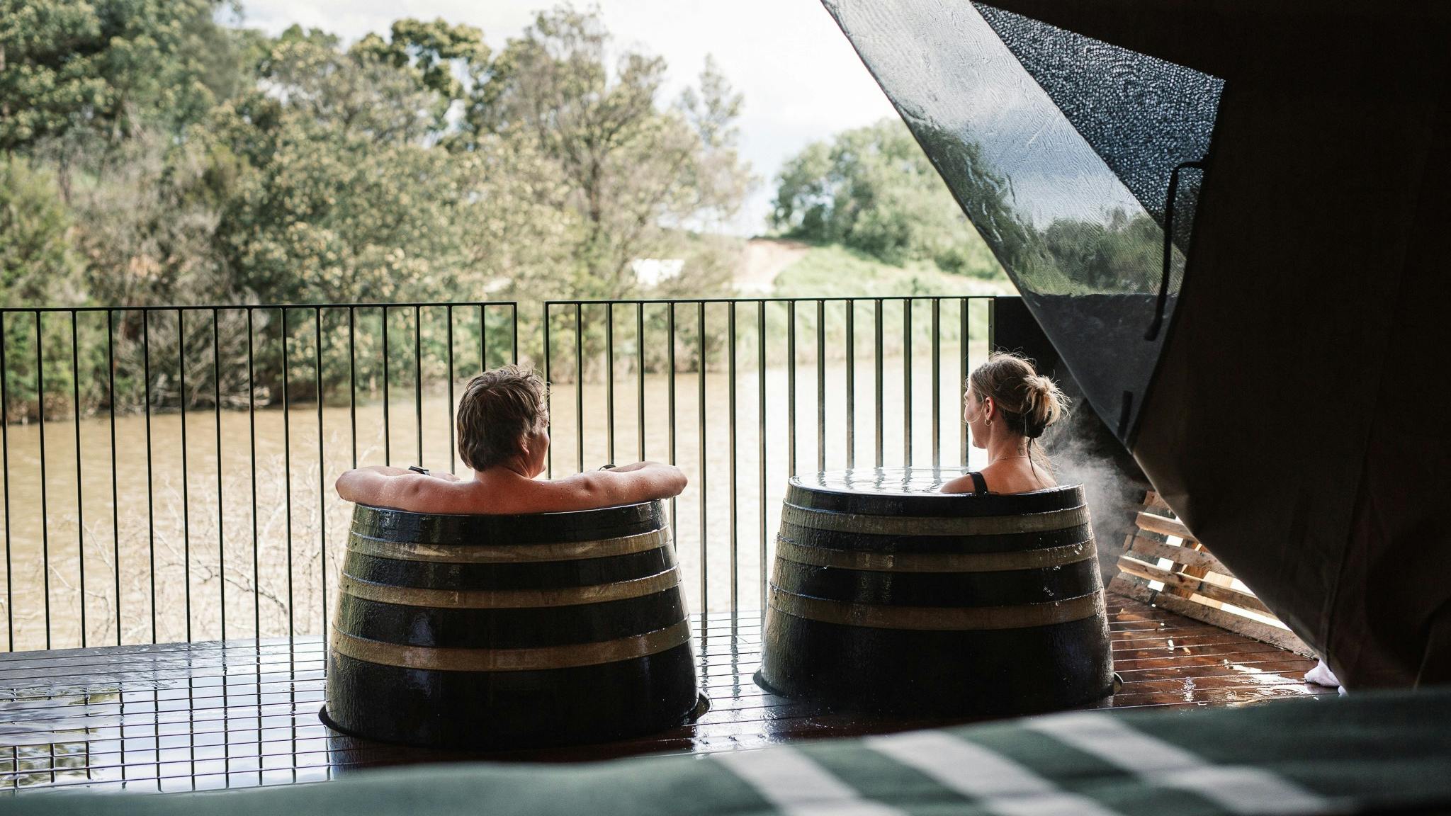 Man and woman bathing in hot springs barrels on their private glamping deck overlooking nature