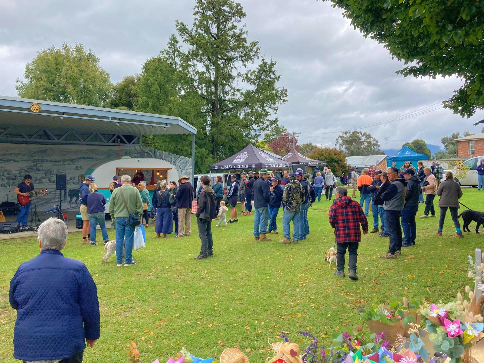 People watching a musician perform with a guitar, market stalls/tents in background