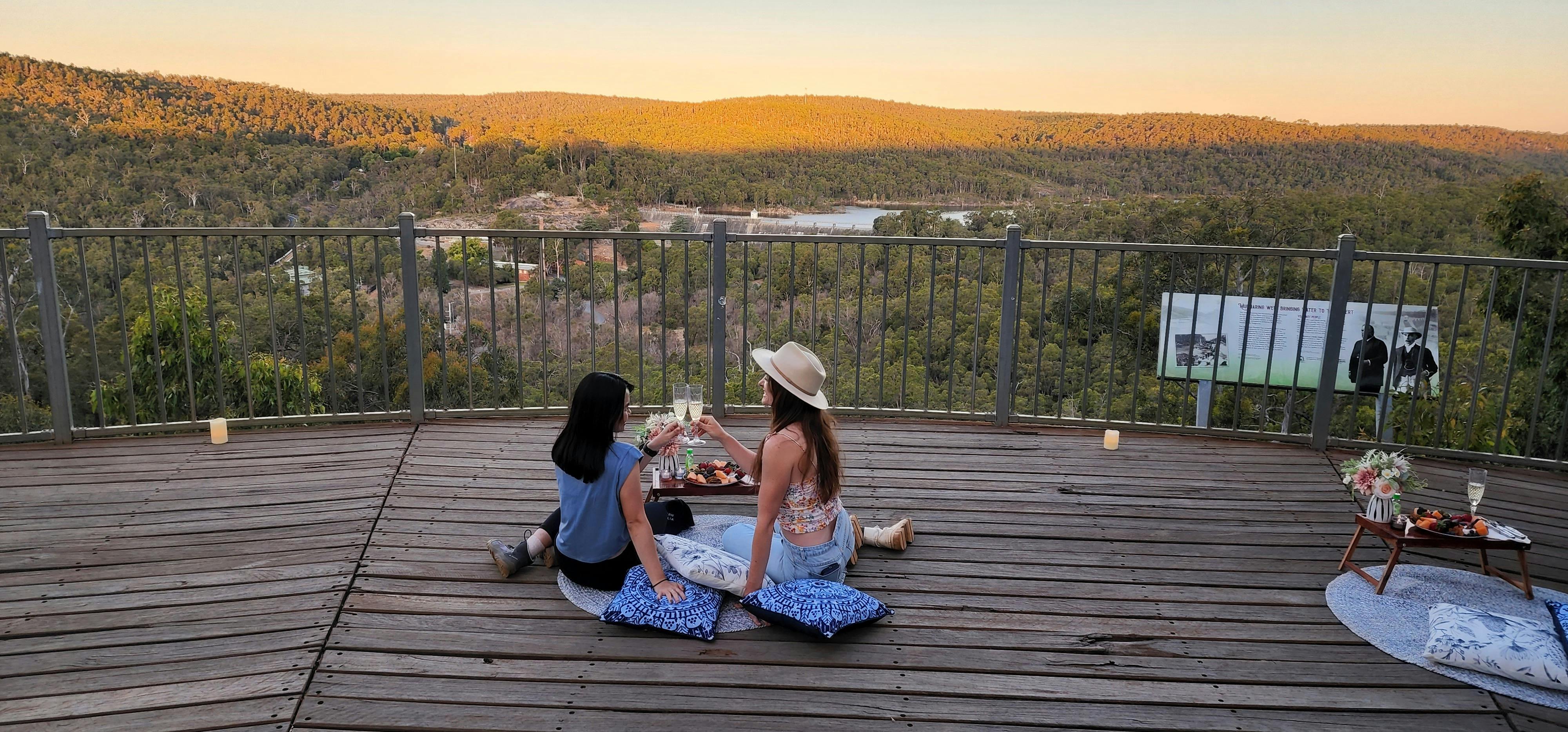 Friends enjoying grazing board on lookout as sunsets over hills in background