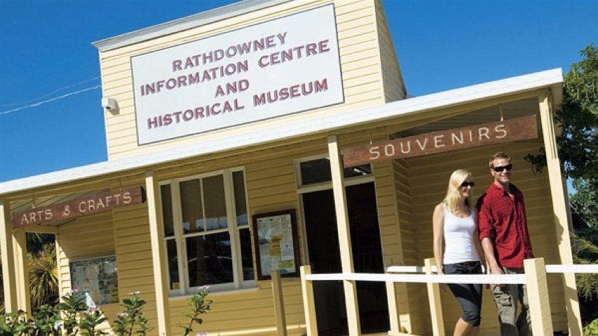Two people walk by exterior of Rathdowney Visitor Information Centre in historic wooden building Two people walk by exterior of Rathdowney Visitor Information Centre in historic wooden building
