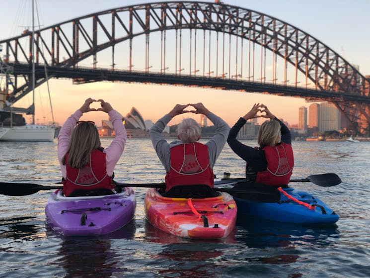 Kayakers enjoying sunrise on Sydney Harbour, looking at the Sydney Harbour Bridge from their kayaks