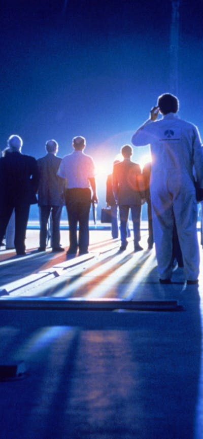 Blue glowy image with the backs of people standing in white lab coats