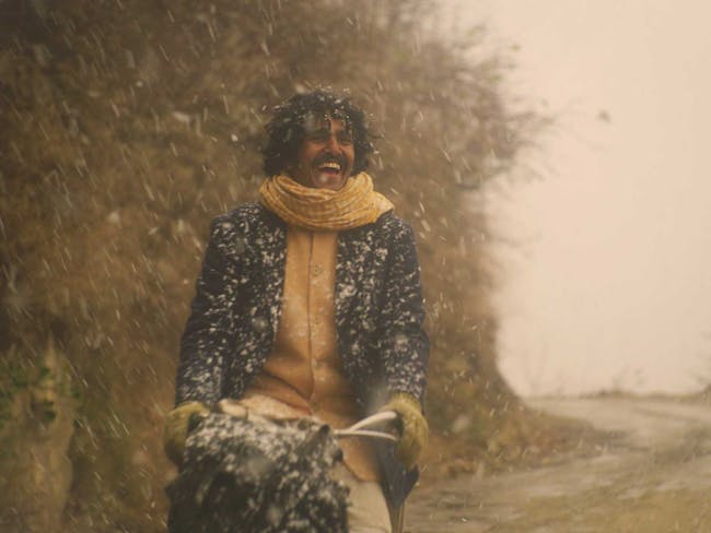 A smiling man, rides a bike through falling snow