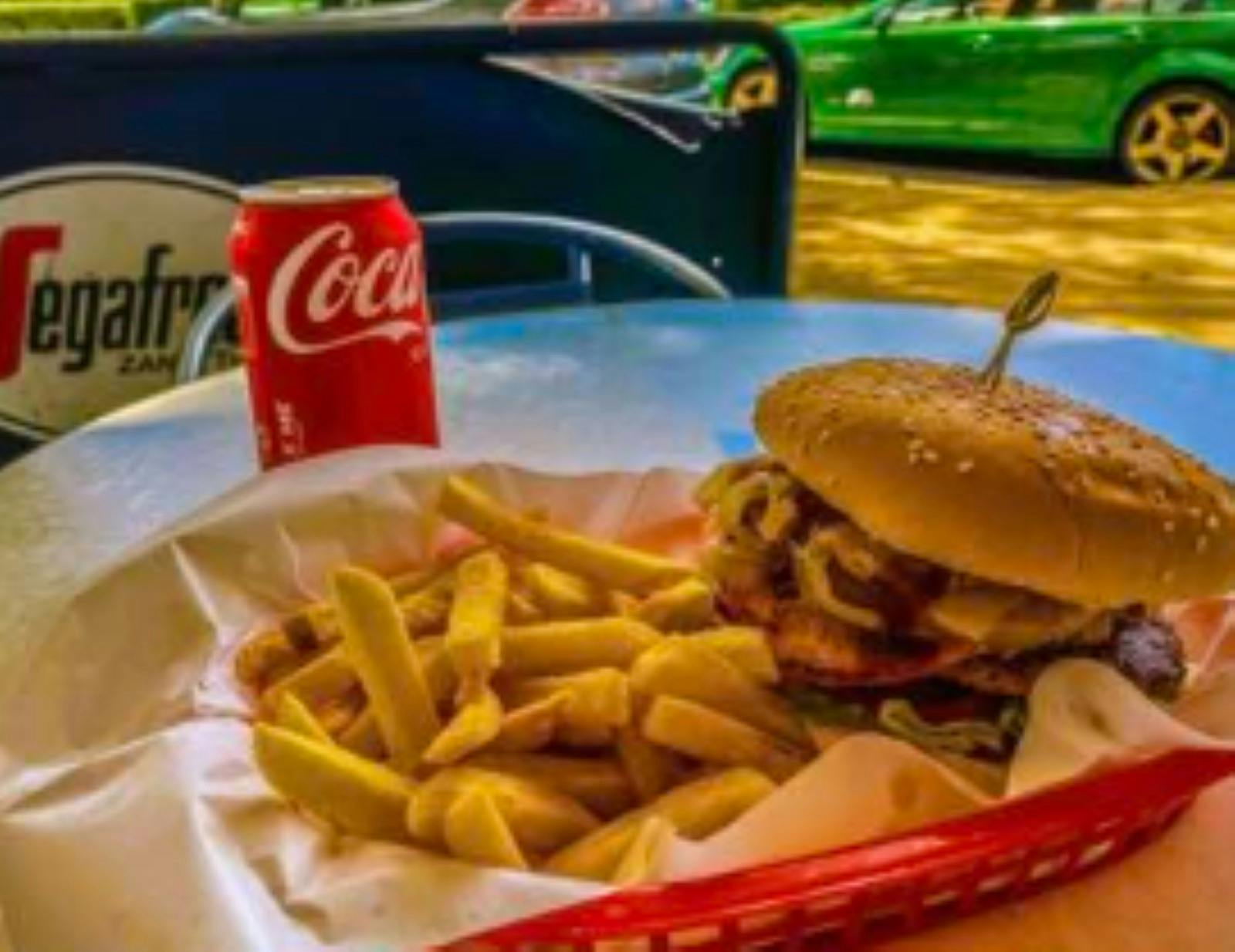 burger fries coke can on an outdoors table with view of road