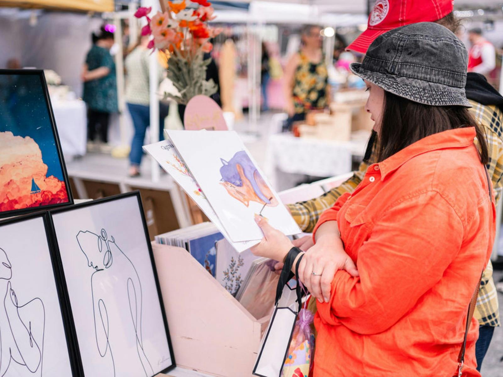 A woman wearing a hat holding and admiring an art print