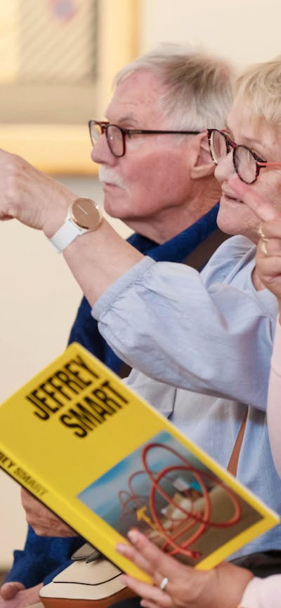 A photograph of 5 people in a gallery space pointing and looking forward