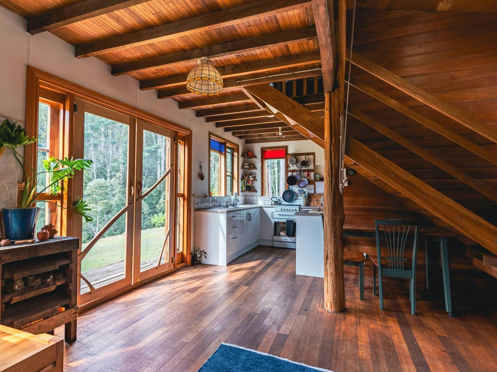 A cosy sunlit cabin kitchen with forest views and vintage chairs.
