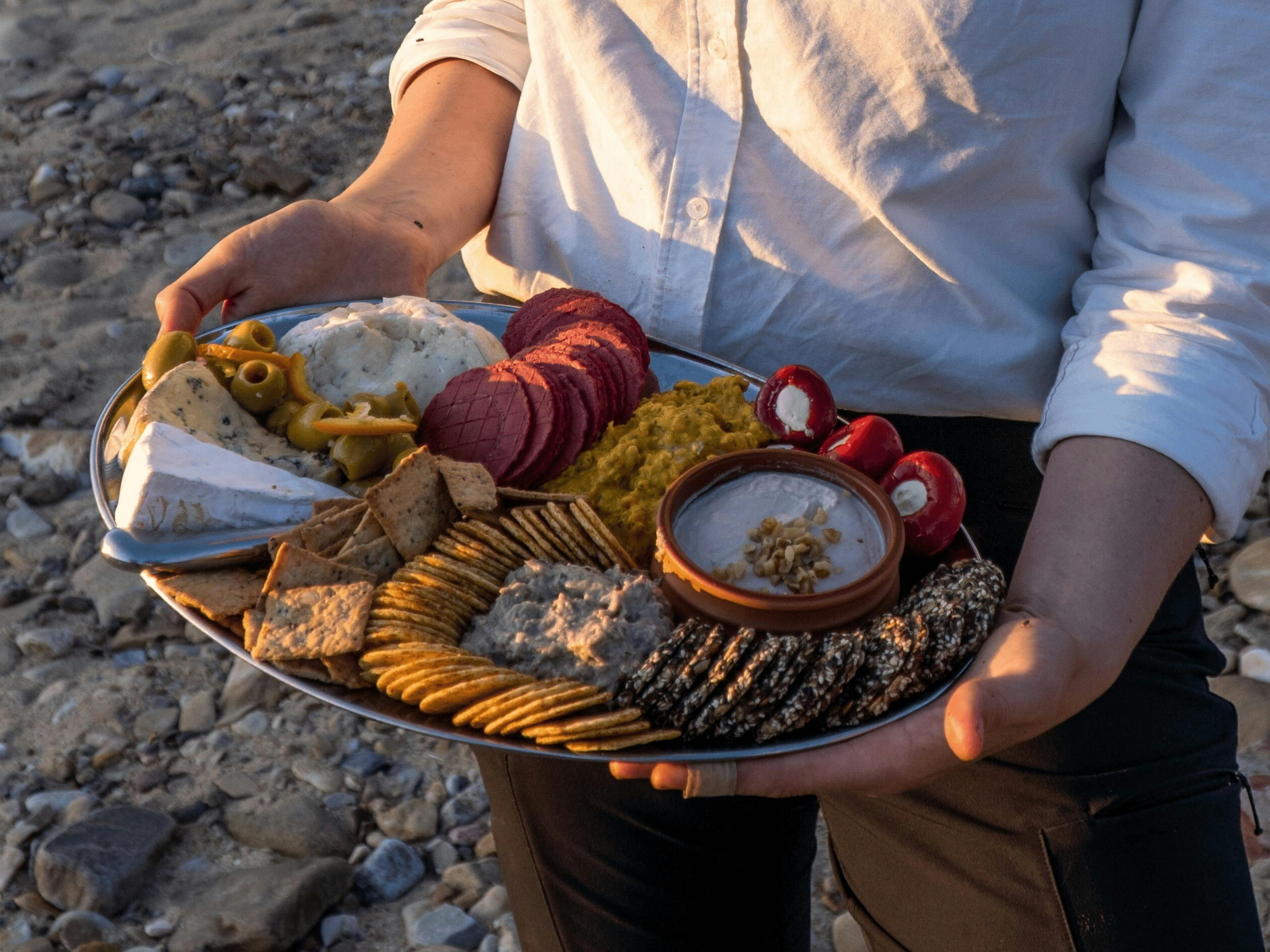 A cheese platter with biscuits, soft cheese, and dip, held by a person in a white shirt