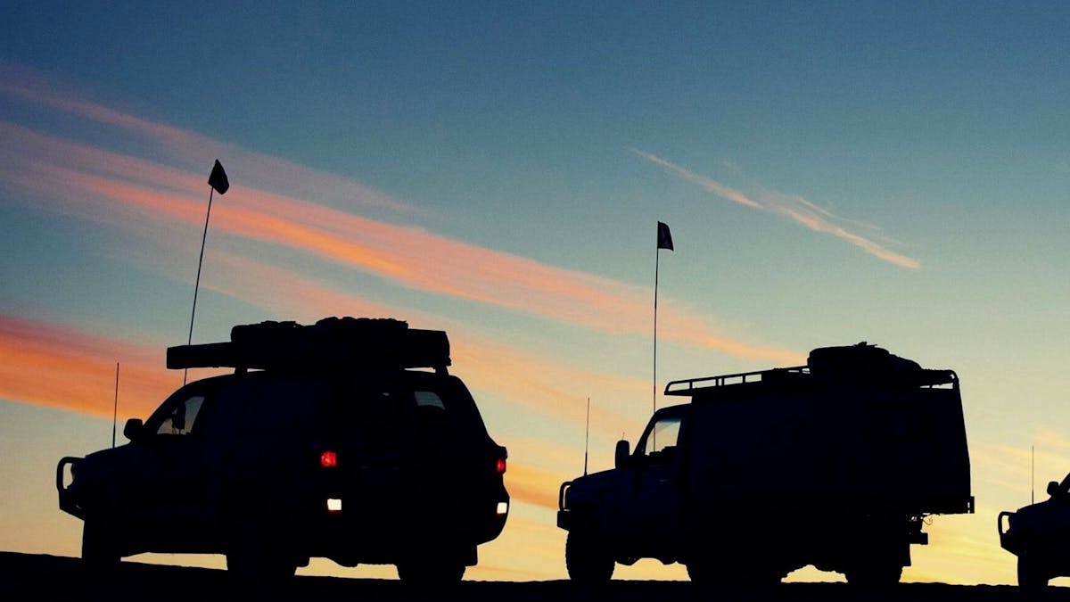 Silhouette of 4x4 cars against an orange and blue sky at sunset.