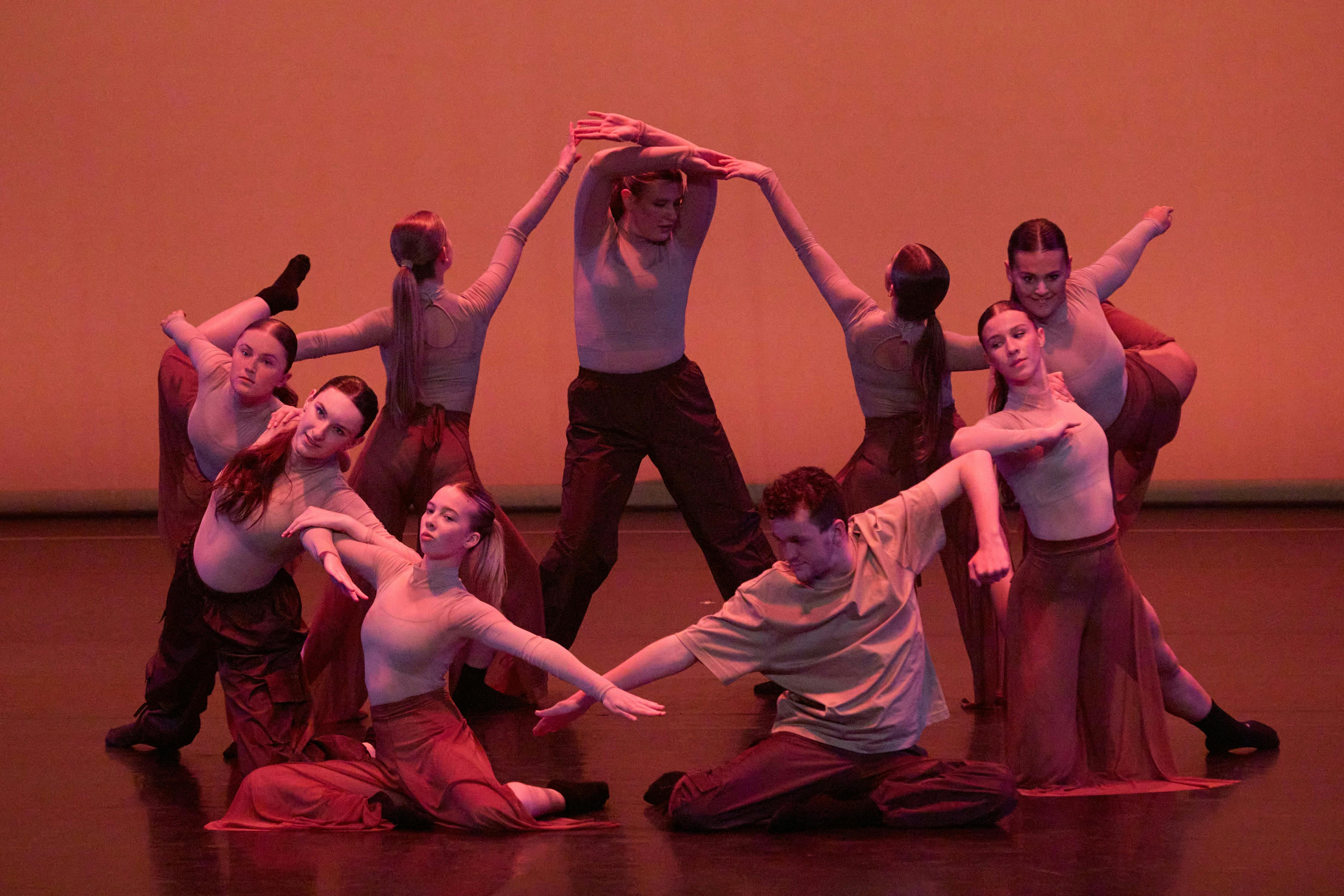 A group of dancers performing a synchronized contemporary piece, with warm lighting.
