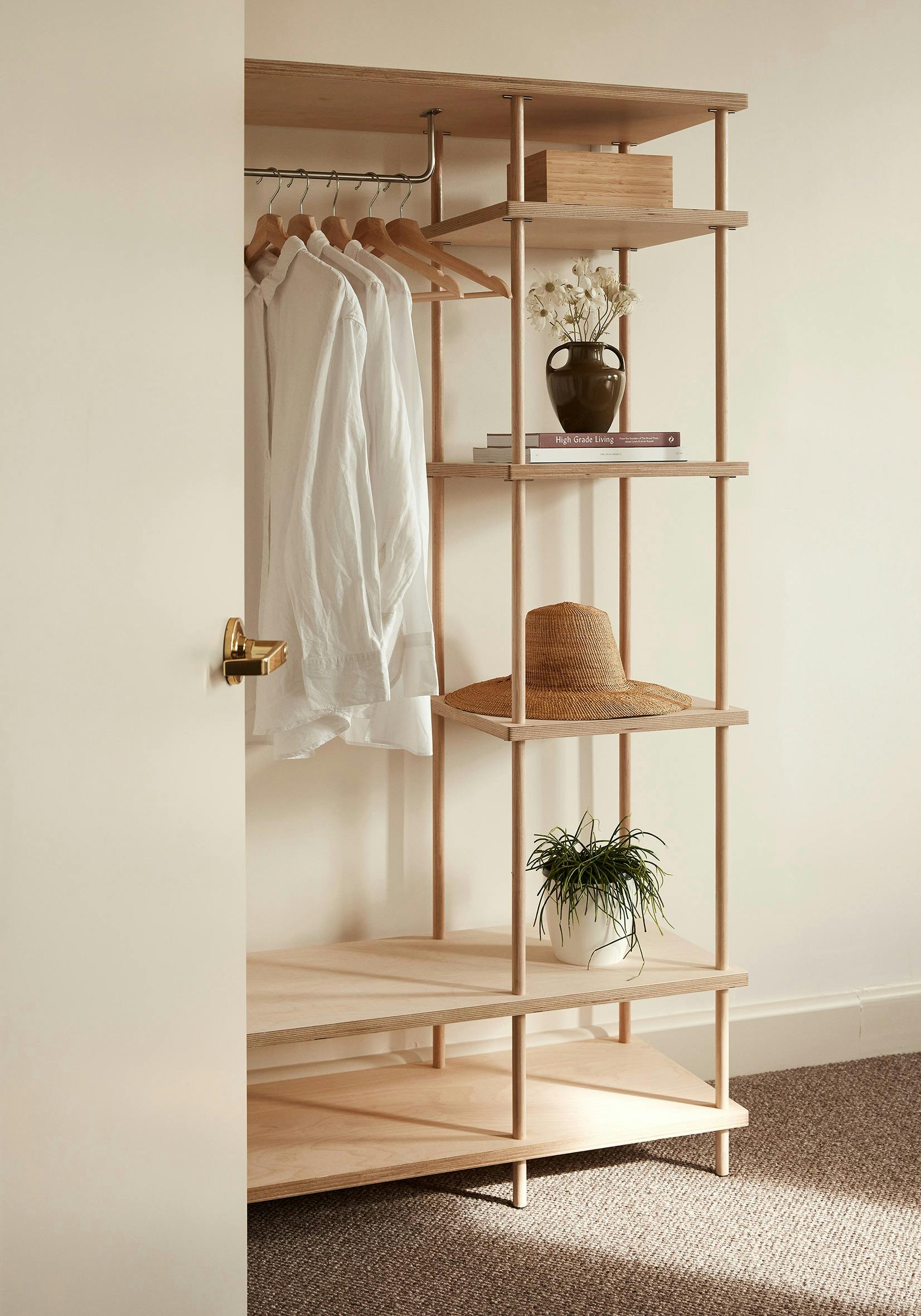 Open wardrobe with light timber shelving, hanging white shirt, and decorative accents