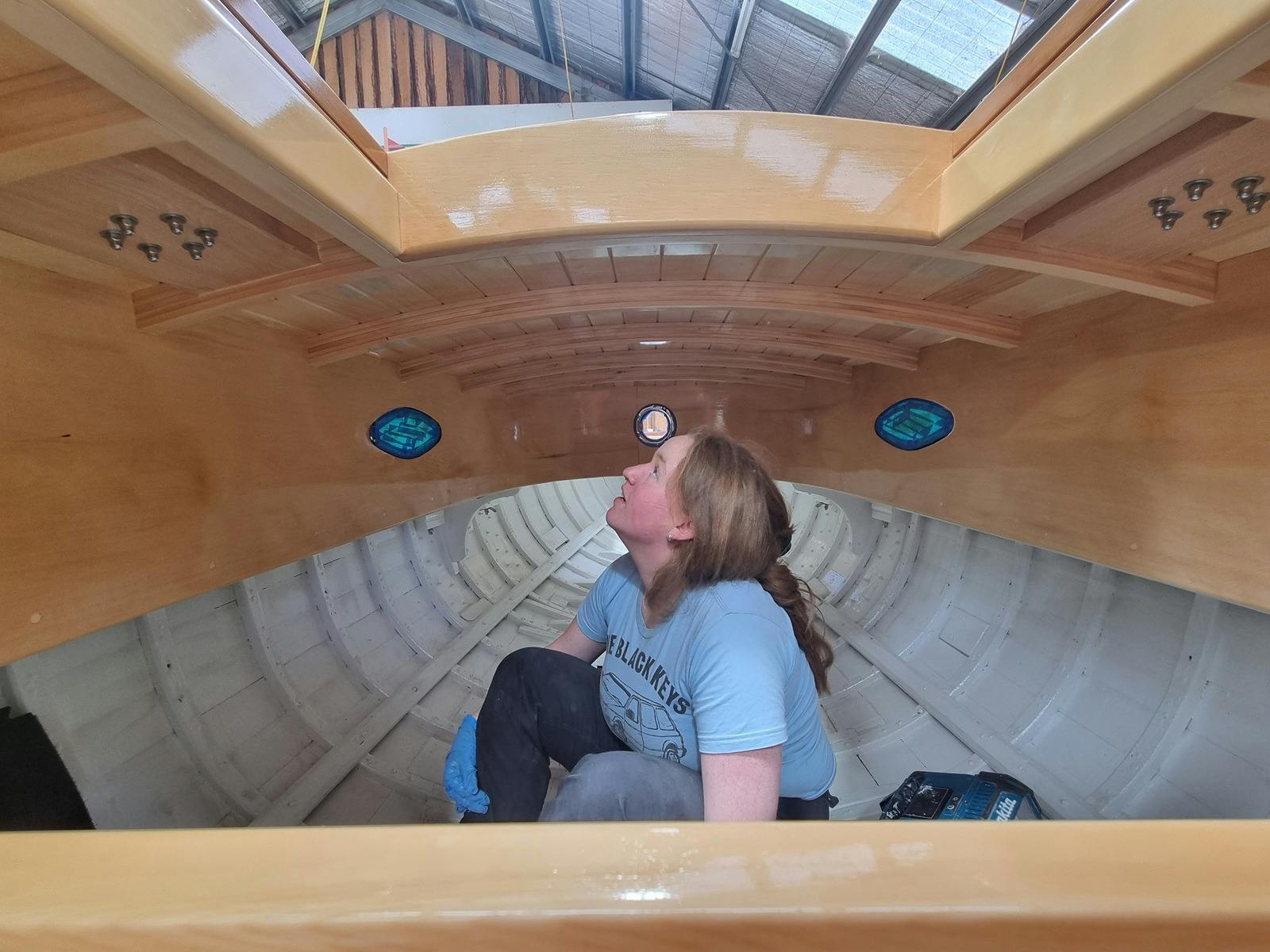 Young person working inside the hull of a wooden boat.