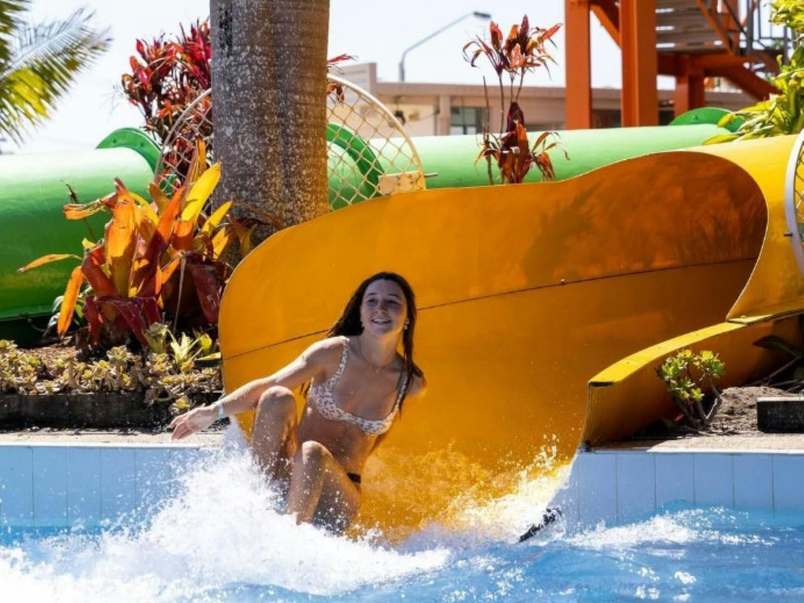 Image of a teenage girl sliding down a yellow waterslide into a pool