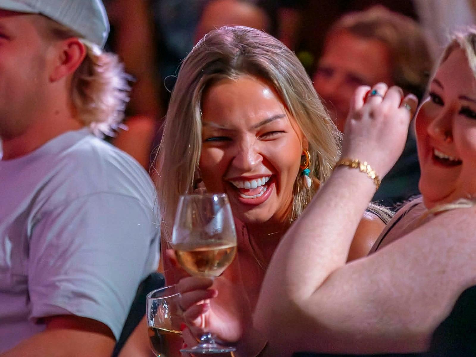 Comedy fans laughing with drinks in hand at a stand-up show in Bondi Junction