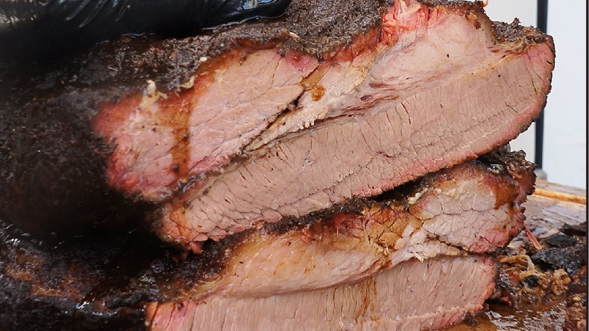 Close-up of sliced smoked brisket showing bark and smoke ring on a wooden board, with juices visible