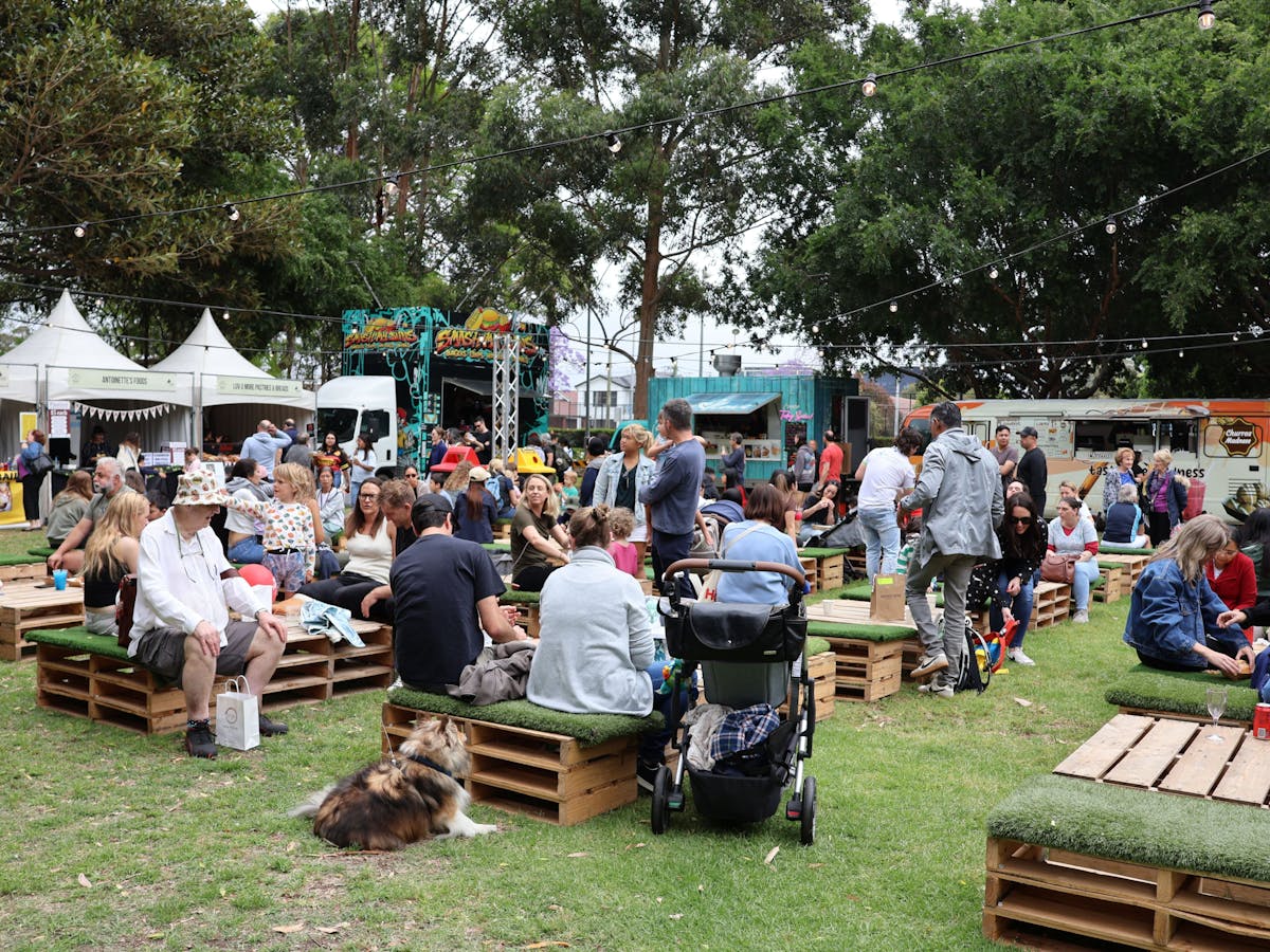 Large group of people sitting and enjoying the local food and beverage stalls at a local park.