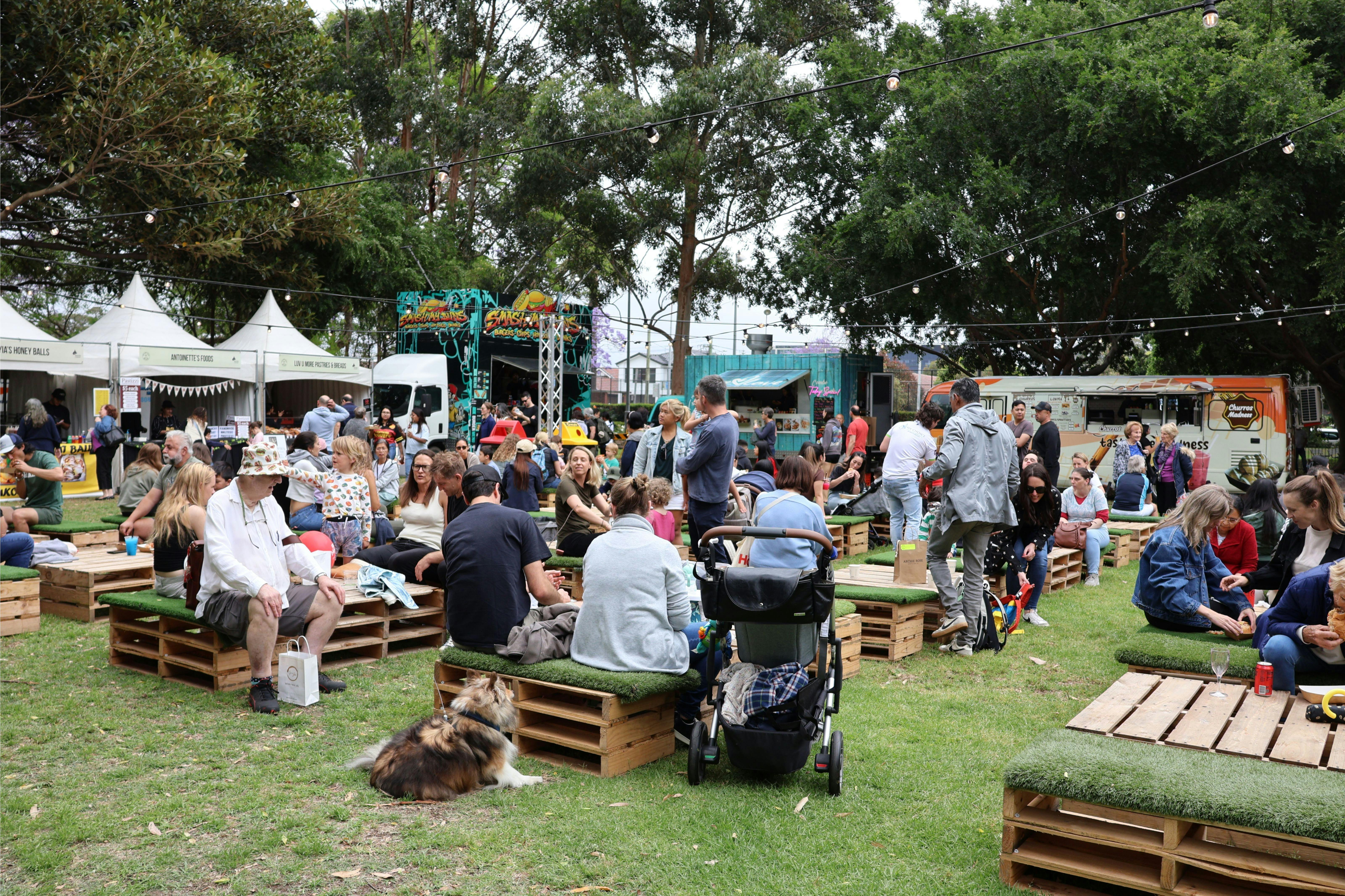 Large group of people sitting and enjoying the local food and beverage stalls at a local park.
