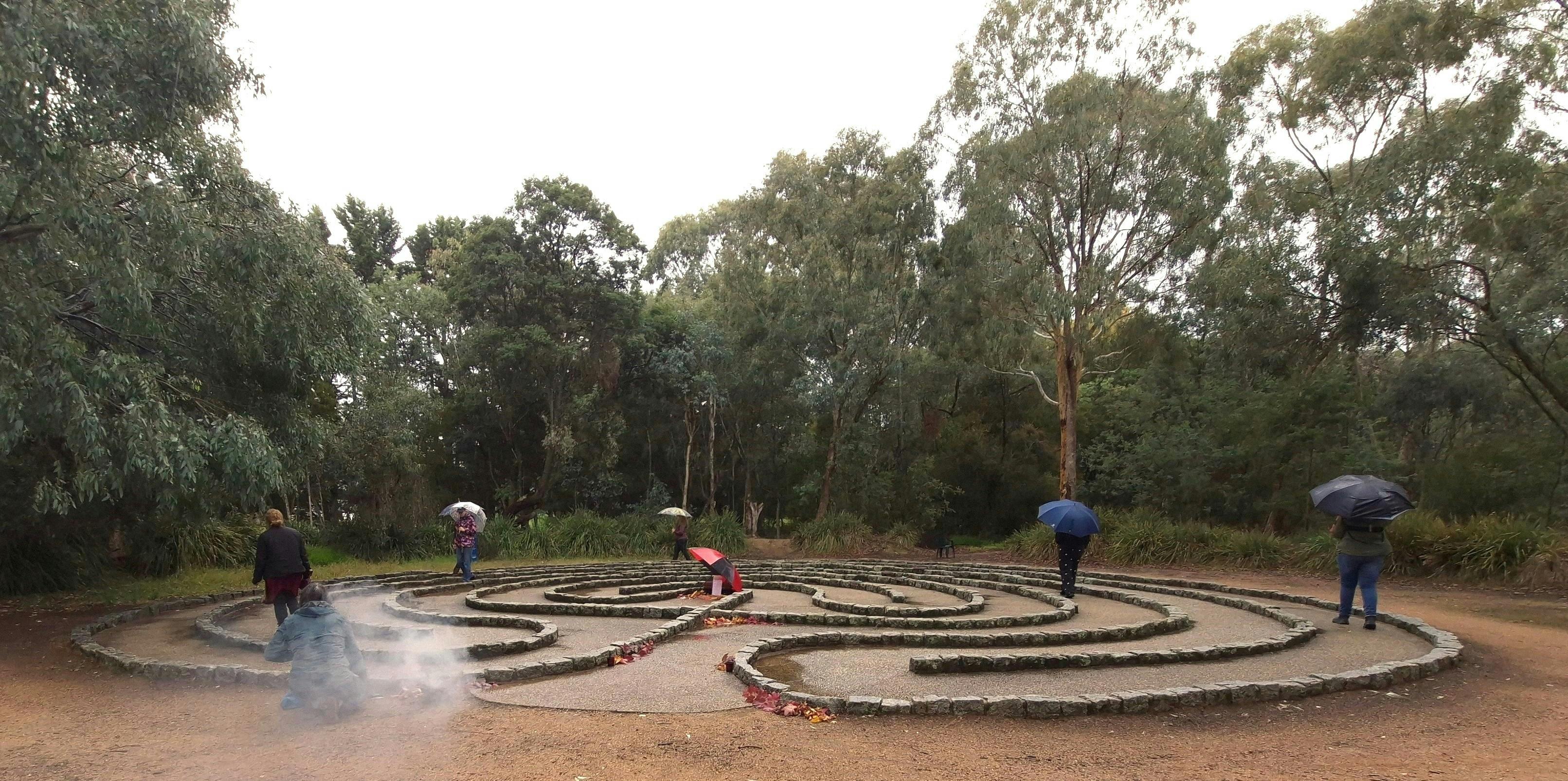 People walking the Beechworth labyrinth in light rain during a guided ritual gathering.