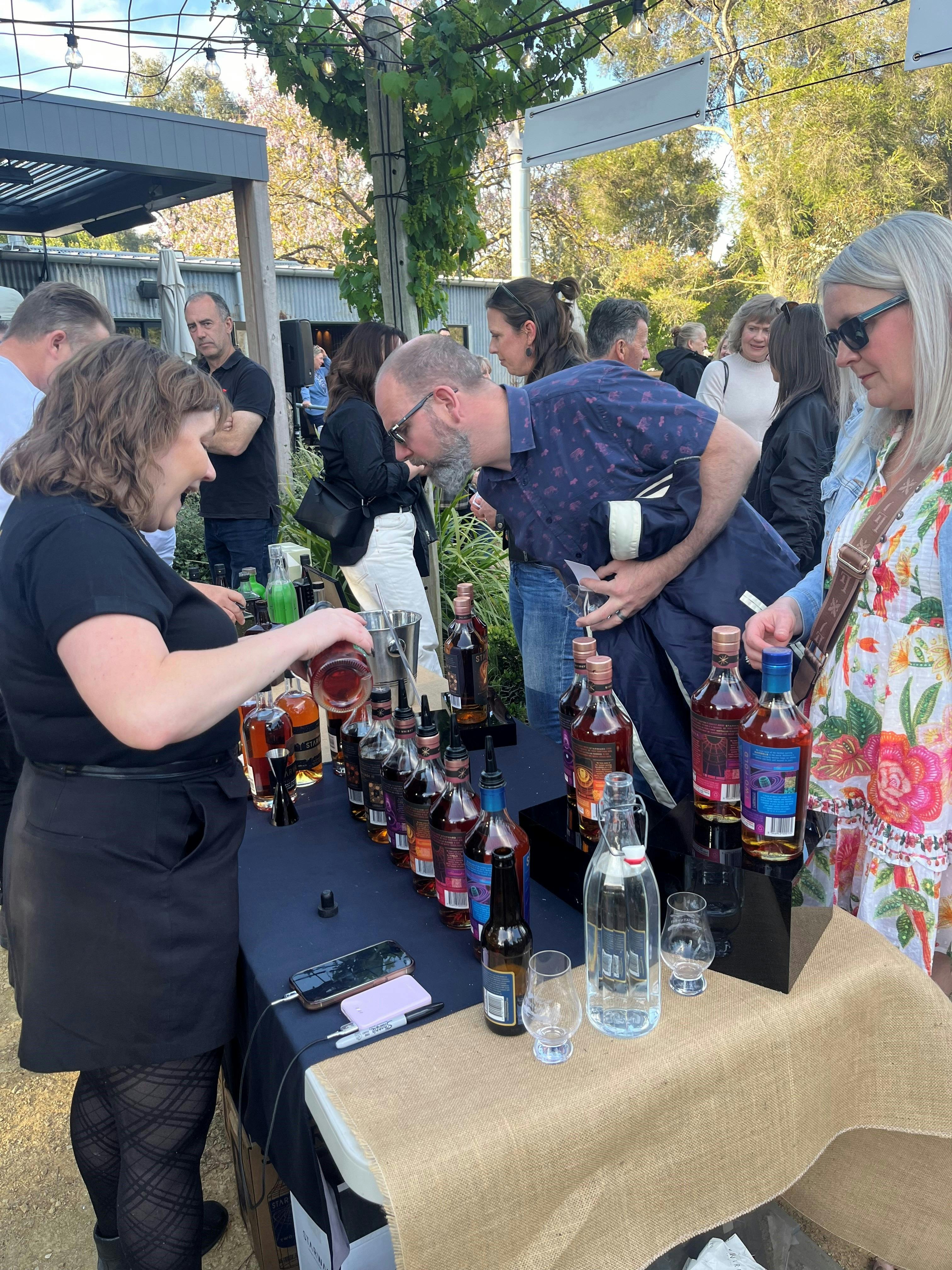 A Starward representative pouring whisky for guests at a busy outdoor tasting table during Whisky by