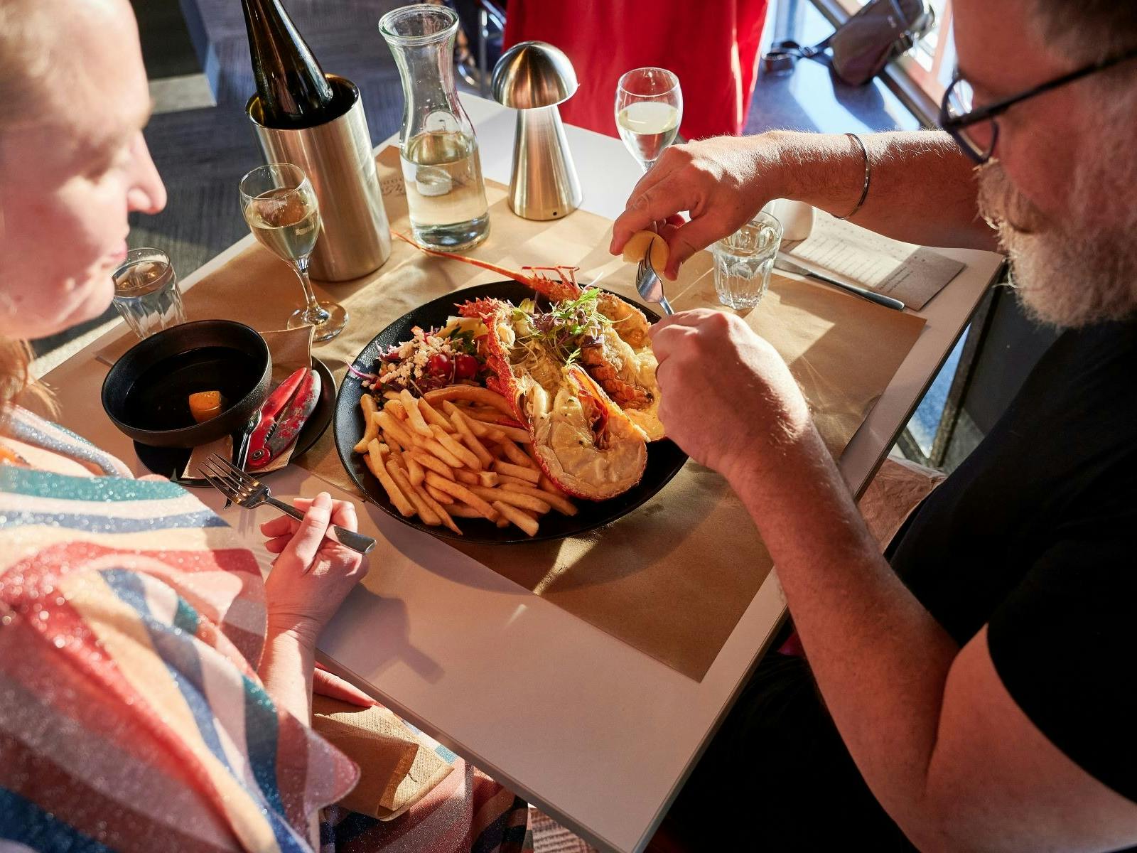 A couple sitting at a table are served a plate of lobster and fresh seafood.