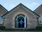 An older man opens the doors to a sandstone hall.