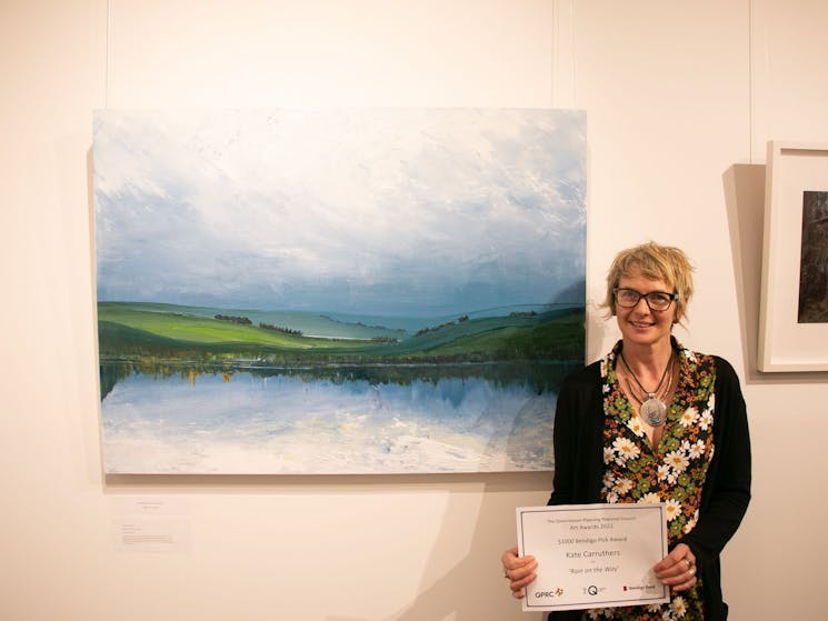Artist standing next to their work holding winning certificate
