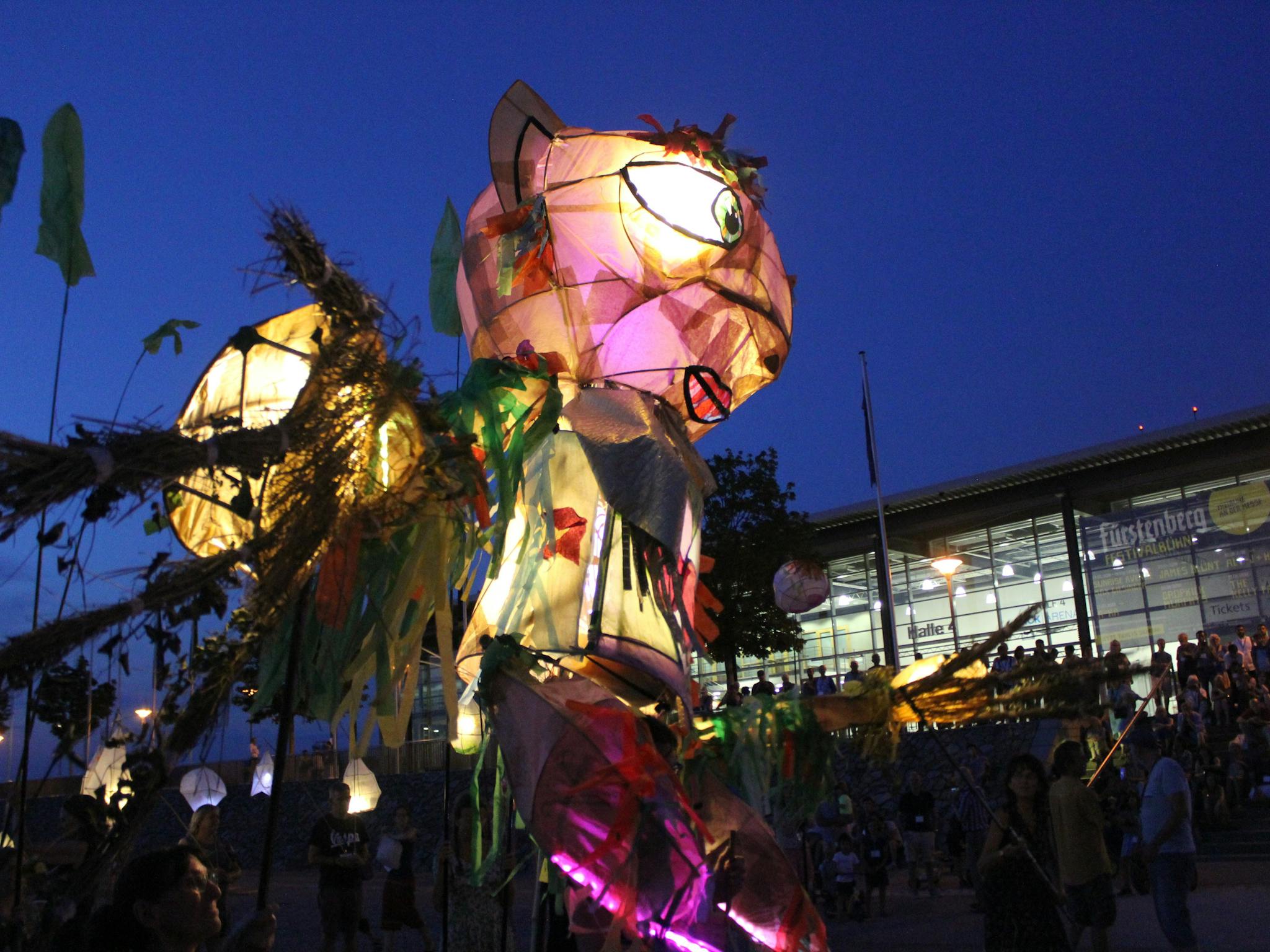 A giant illuminated puppet walks down a street crowded with people