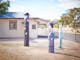 Bollards carved and painted to look like people, train station, railway tracks, trees, sunny day.