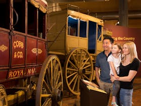Mum, Dad and daughter looking at a mail coach, part of the National Carriage Collection