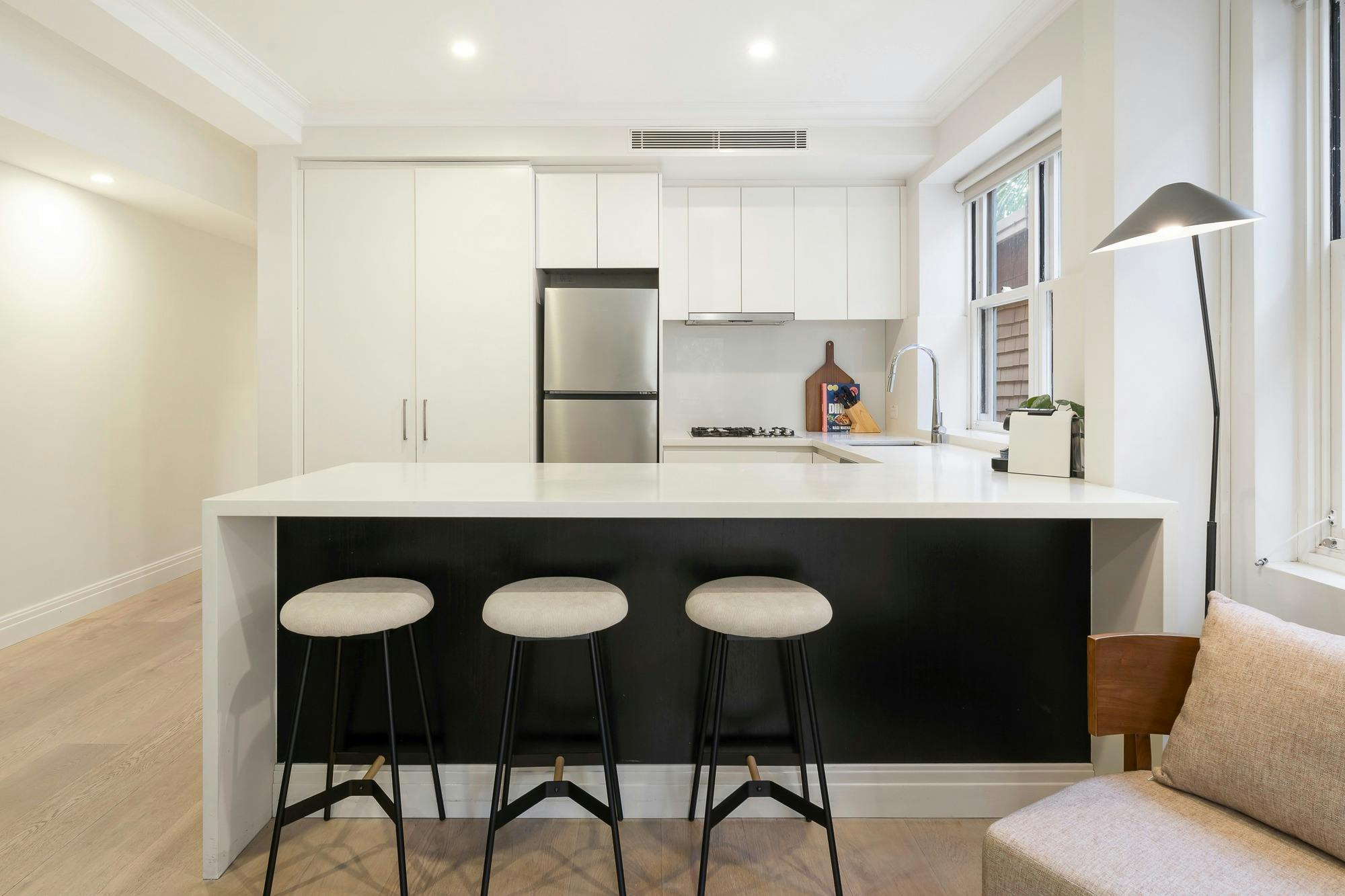Modern kitchen with stainless steel appliances, white cabinets, island bench with 3 white barstools.