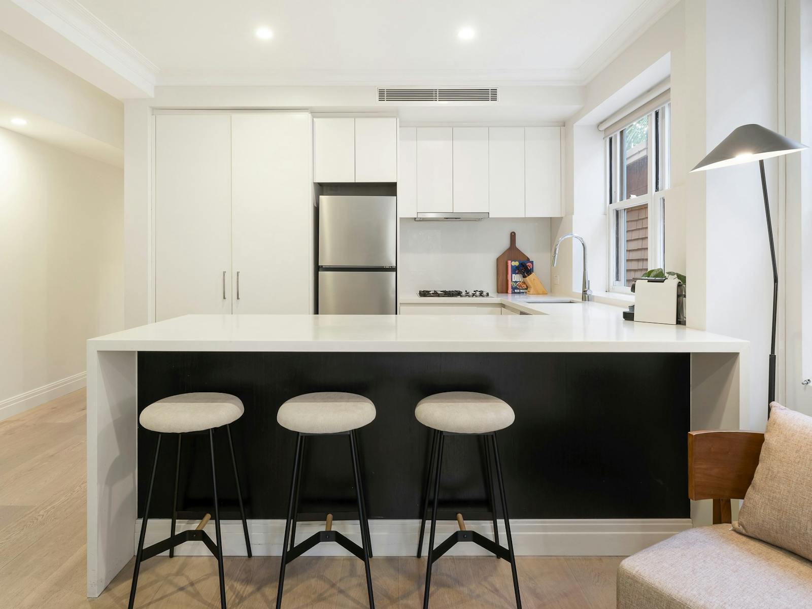 Modern kitchen with stainless steel appliances, white cabinets, island bench with 3 white barstools.