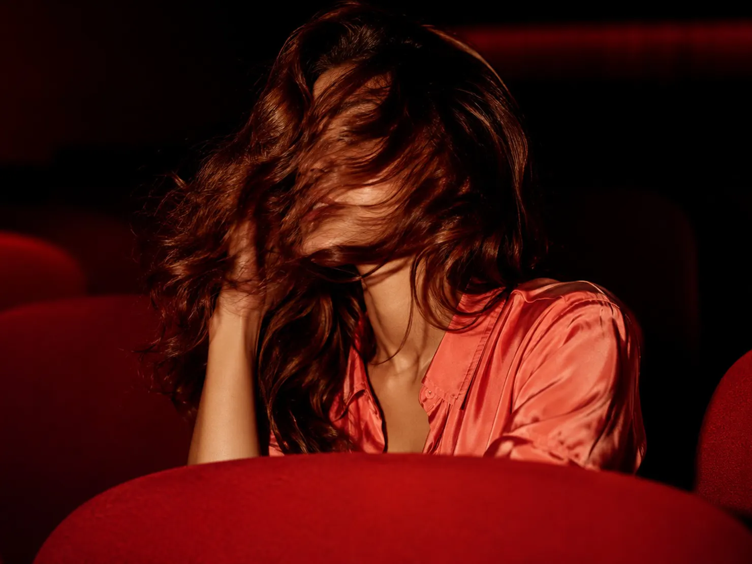 woman in theater with red theater seats and brunette hair across face