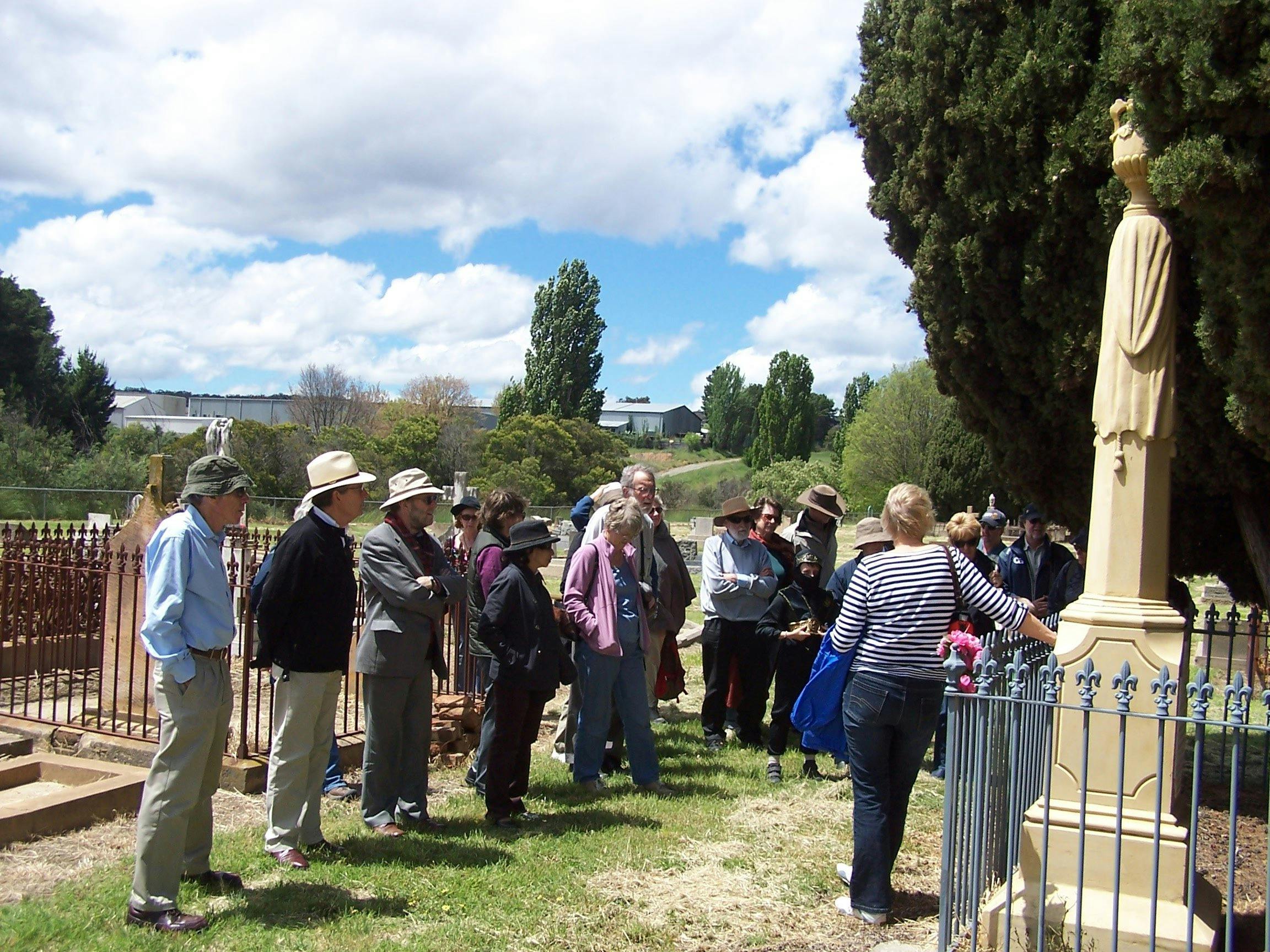Group of people standing in old cemetery with large cypress and stone tombstones