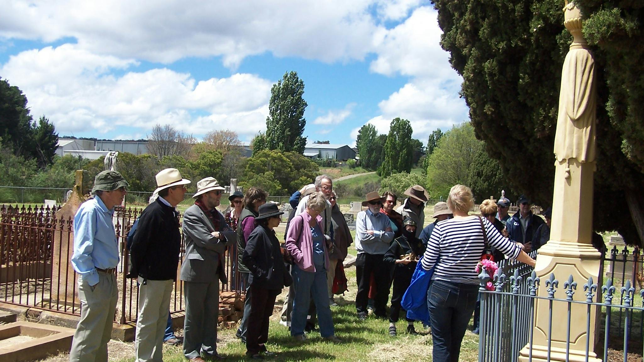 Group of people standing in old cemetery with large cypress and stone tombstones