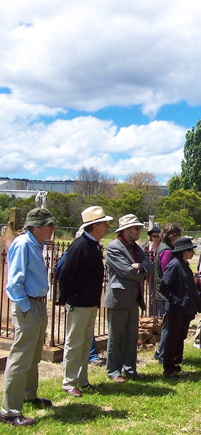 Group of people standing in old cemetery with large cypress and stone tombstones