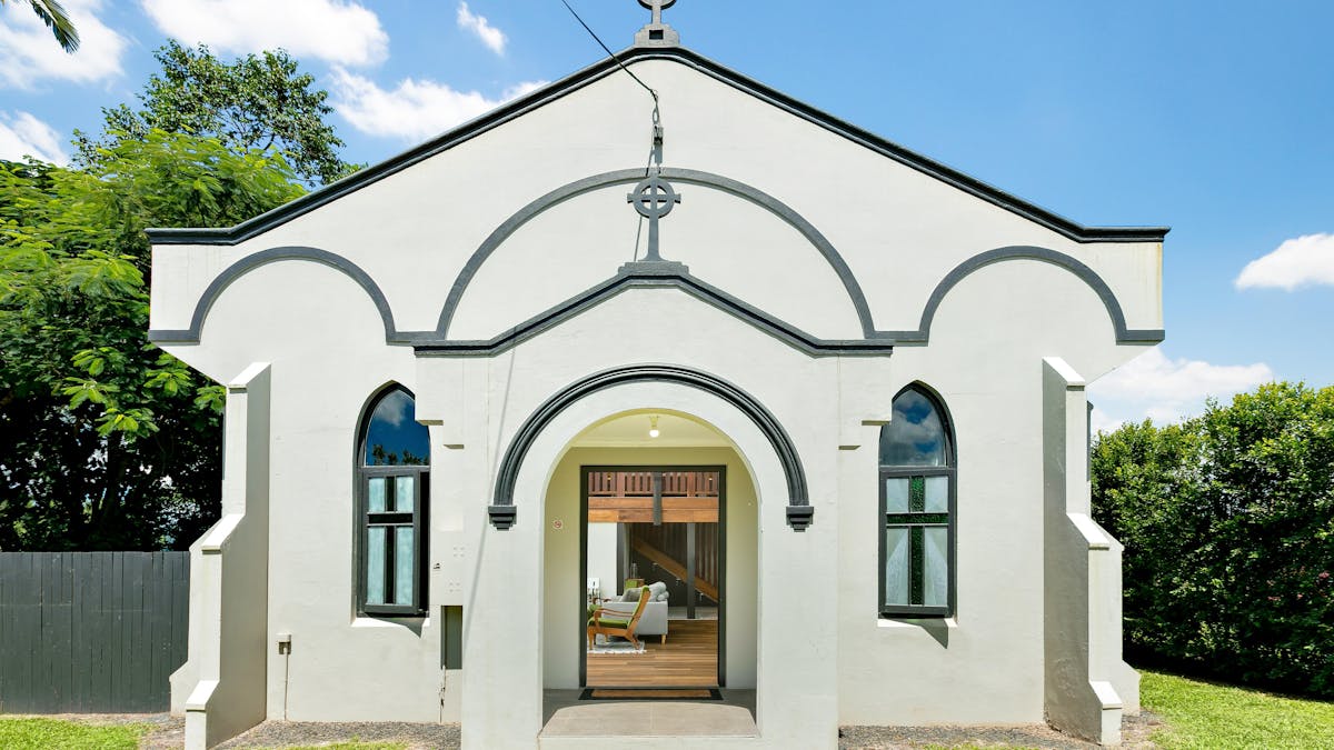 Shows the exterior of an old restored church on a sunny day. The church is white with black trim.