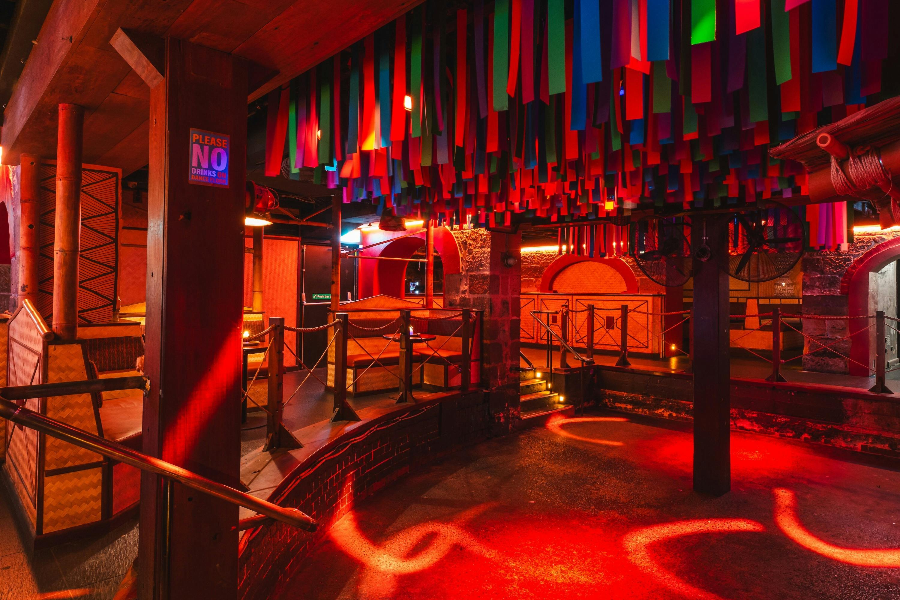 A nightclub interior with a sunken dance floor lit in red light