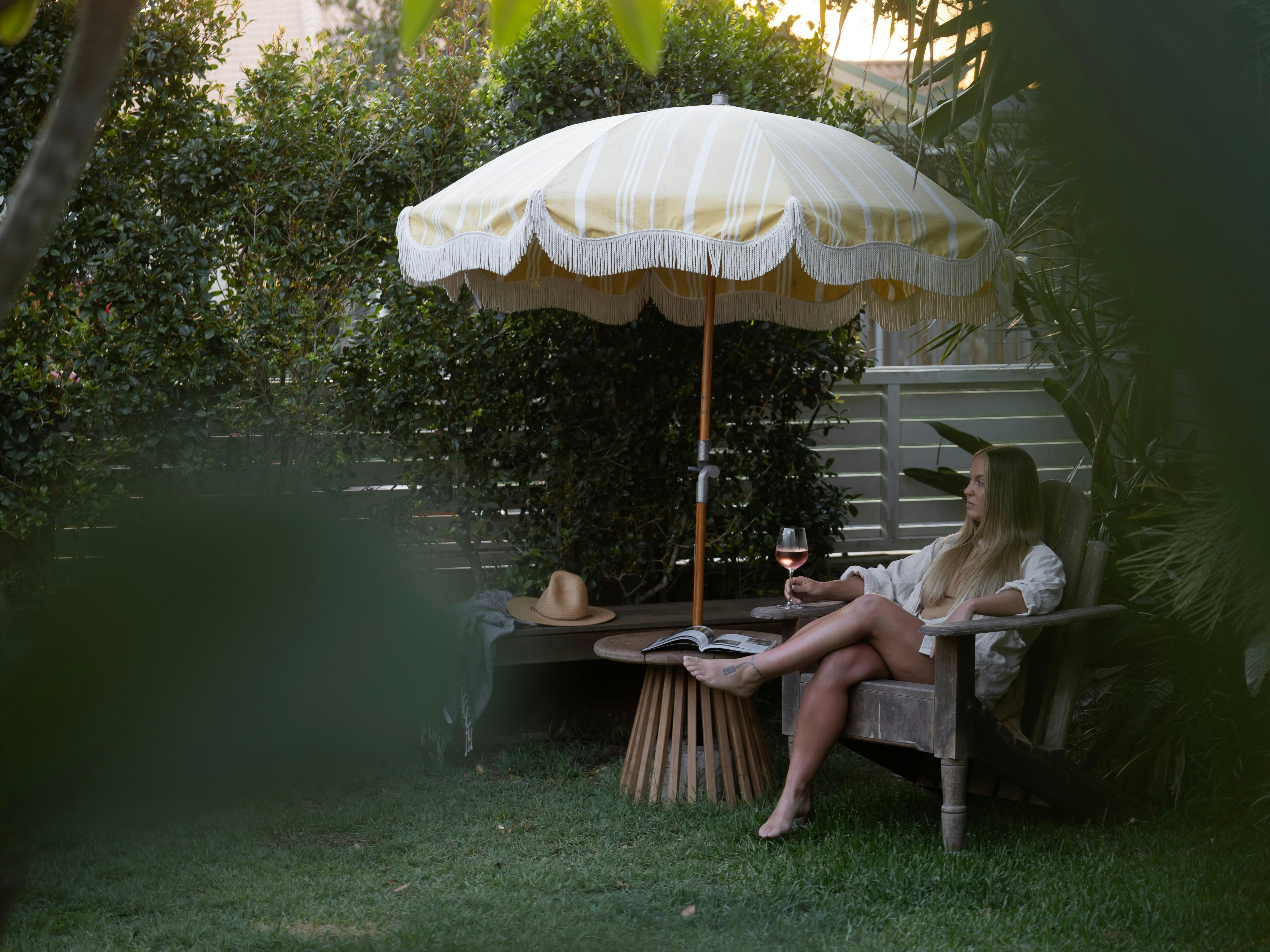 Female Guest enjoying a glass of rose in the garden with a yellow striped beach umbrella