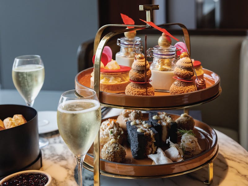 A two-tier stand of sweet and savoury high tea pastries and delicacies. Sparkling wine in foreground
