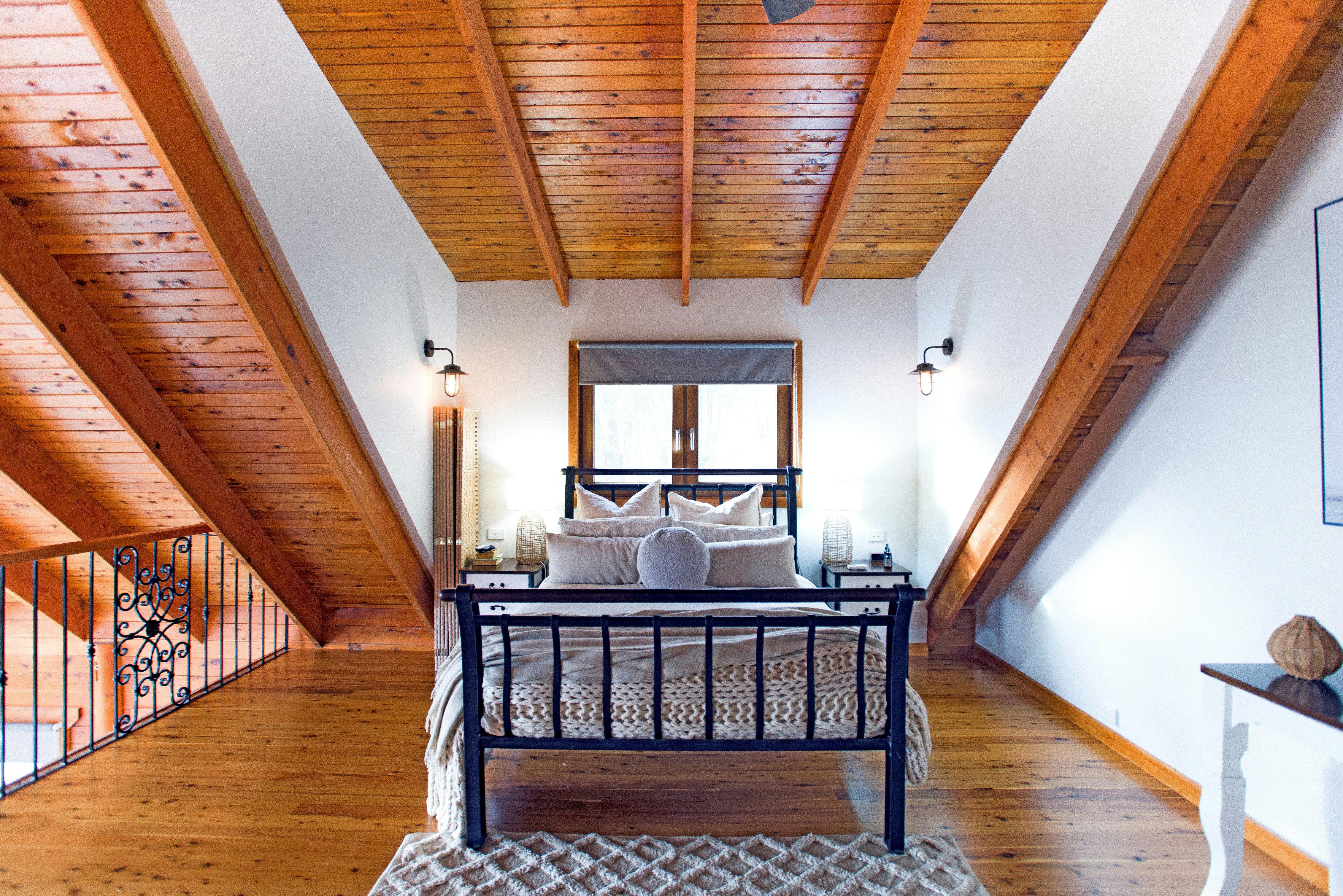 Loft bedroom with timber ceiling, iron bed, and warm lighting.